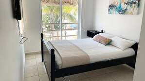 A bedroom with a bed, a nightstand, a TV mounted on the wall, and a window with a view of greenery outside. - Casa en nuevo Altata, Punta Esmeralda Grand (Nuevo Altata)