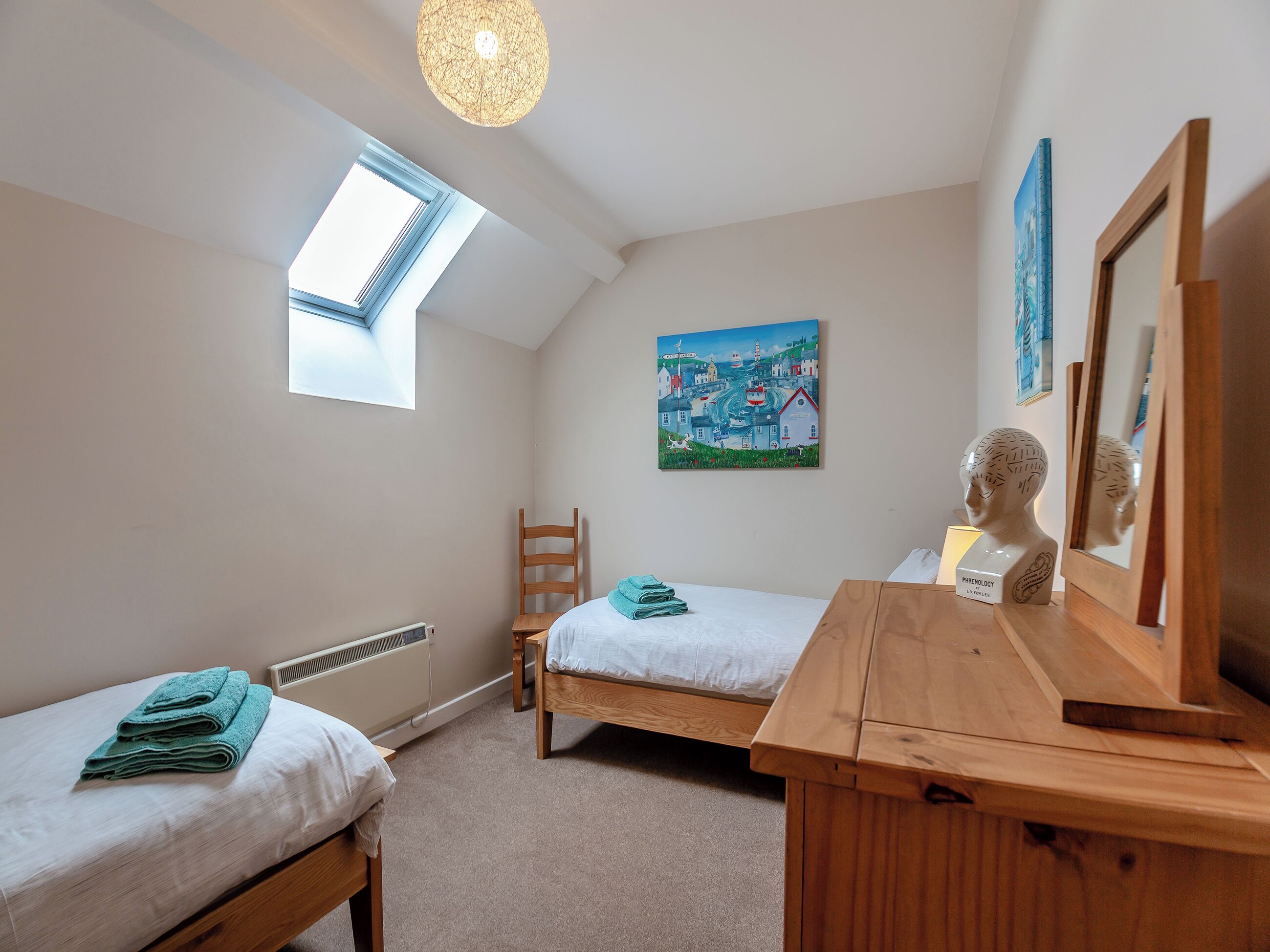 A bedroom with two beds, a wooden dresser, a painting, a mirror, and a skylight.