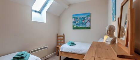 A bedroom with two beds, a wooden dresser, a painting, a mirror, and a skylight.