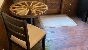 Interior acogedor de una cabaña con paredes de madera, una mesa redonda con sillas, una puerta con ventana y un pequeño armario.
