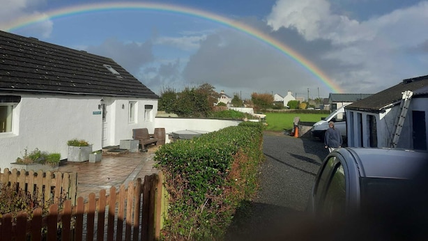 Un quartier résidentiel avec des maisons, un arc-en-ciel et une voiture garée.