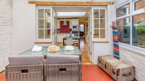 A compact kitchen with white cabinets, a red tiled backsplash, and a dining area with wicker furniture. - 5 bedroom accommodation in Weymouth (Weymouth)