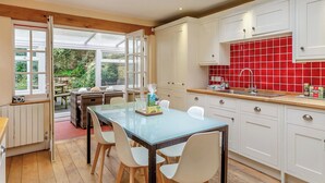A modern kitchen with white cabinets, a red backsplash, and a glass dining table with chairs. - 5 bedroom accommodation in Weymouth (Weymouth)