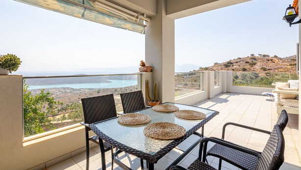 En balkon med et glasbord og stole, udsigt over et bjerrelandskab, samt en potteplante.