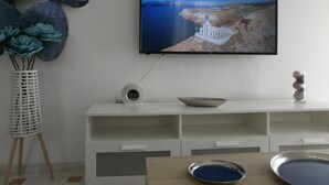 A modern room with a flat-screen TV mounted on the wall, a white console table with a bowl and decorative items, and a vase with blue flowers.