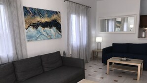 A modern living room with a grey sofa, a wooden coffee table with two blue trays, a dark blue sofa, a small table with a lamp, and a large abstract painting on the wall.