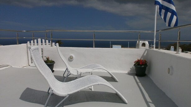 A rooftop terrace with white lounge chairs and potted plants.