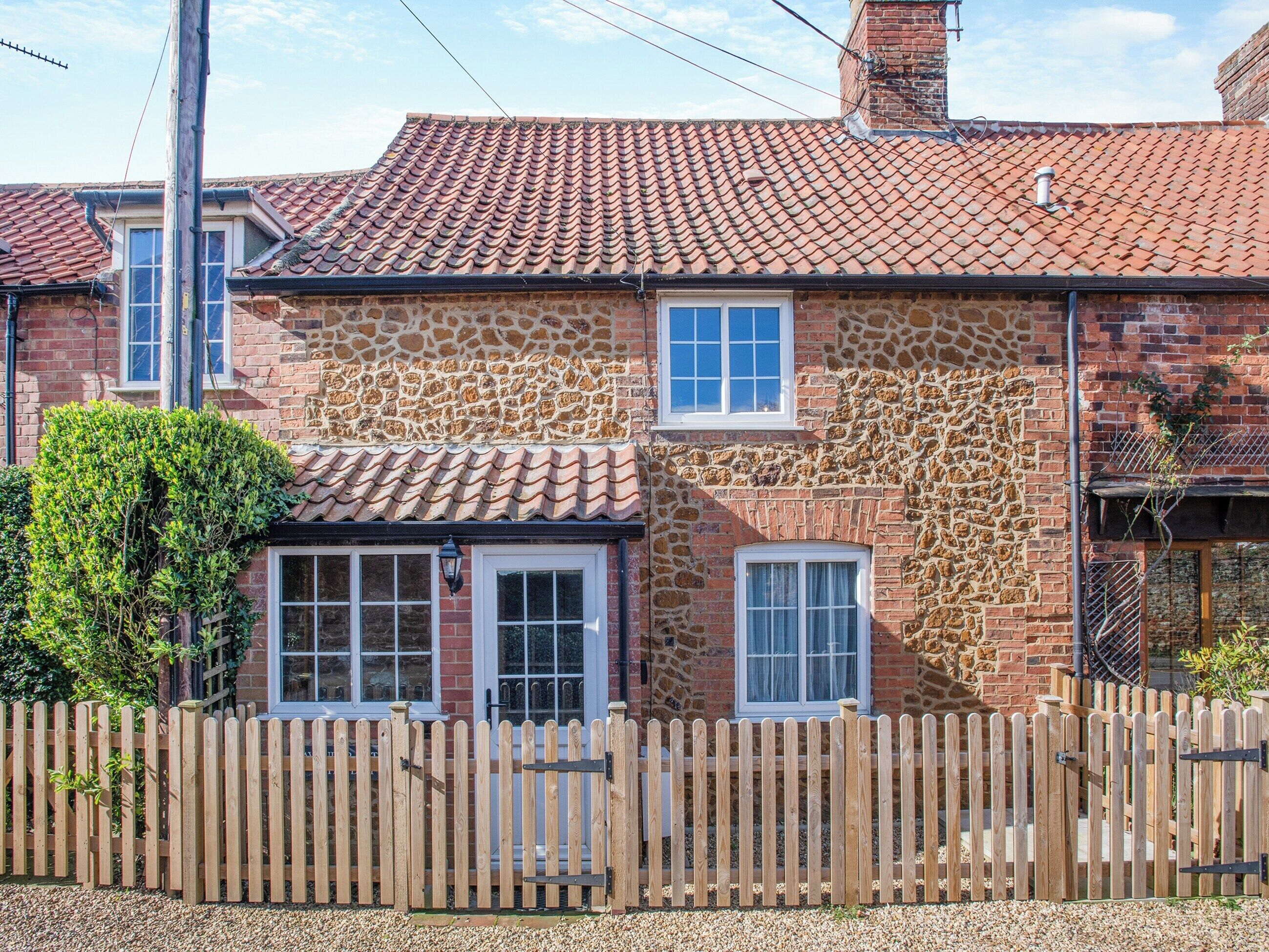 A stone house with a tiled roof, a wooden fence, and a small garden.