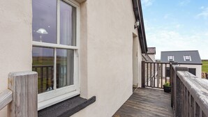 Een balkon met houten leuning, een raam met witte omlijsting en een uitzicht op een huis op de achtergrond.