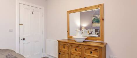 A bedroom with a wooden dresser, a white door, a radiator, and a mirror on the wall.