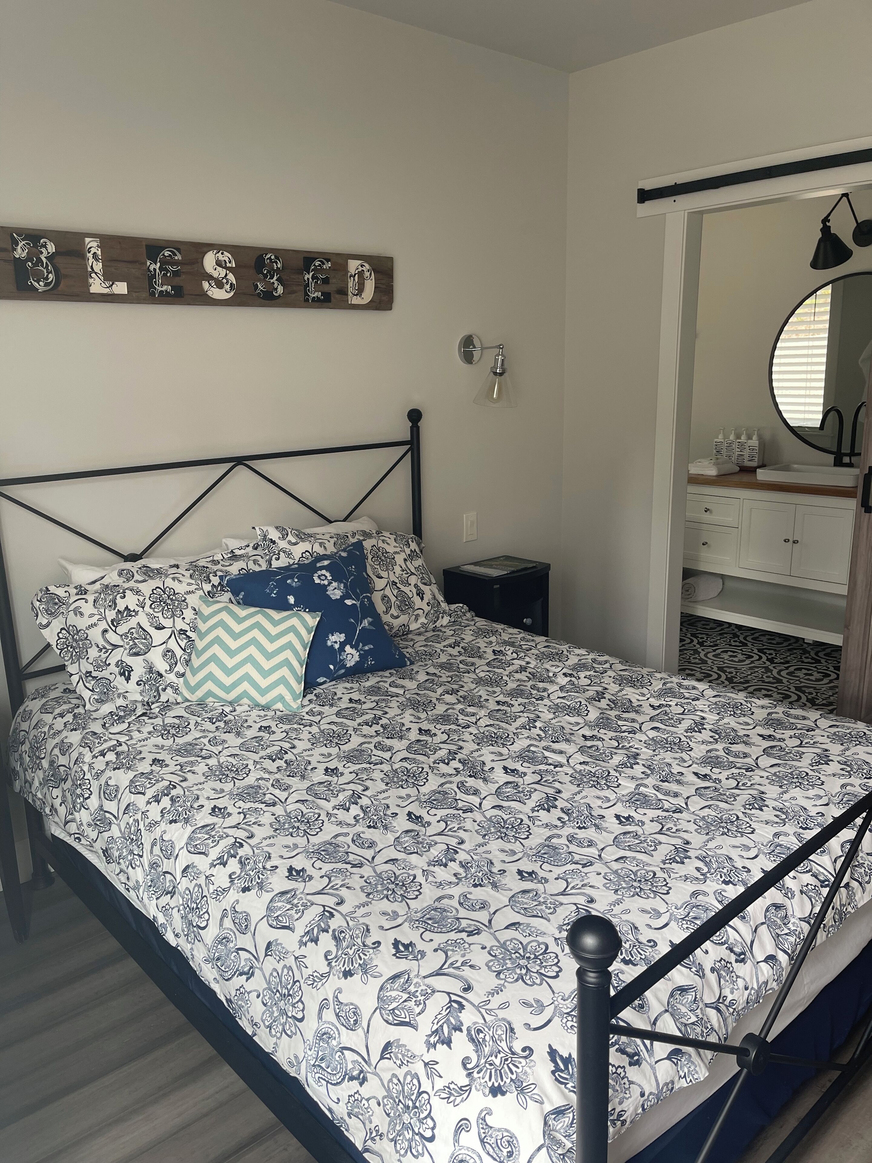 A bedroom with a bed, a nightstand, a dresser, a mirror, and a wall-mounted light fixture.