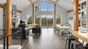 A spacious living area with a fireplace, a dining table, and a large window offering a view of the outdoors. - Huge game room, Hot tub, Sleeps 16+ with Bonus loft, ATV Snowmobile Trails (Cle Elum)