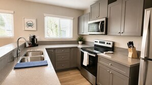 A modern kitchen with grey cabinets, a stainless steel sink, a microwave, and a stove. - Spacious South Bay Condo (Torrance)