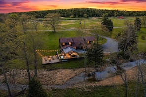 A house with a large deck, surrounded by trees and a river. - Creekside Ranch - Big Yard, Hot Tub, Fire Pit, Game Room, Pet-Friendly (Broken Bow)