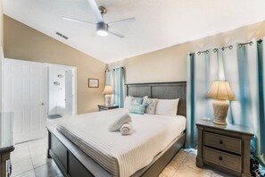 A hotel room with a bed, nightstands, a ceiling fan, and a door. - Cozy Oasis 5BR Near Disney with private pool (Kissimmee)