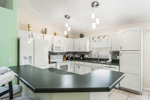 A modern kitchen with white cabinetry, a central island, and a hanging light fixture. - Cozy Oasis 5BR Near Disney with private pool (Kissimmee)