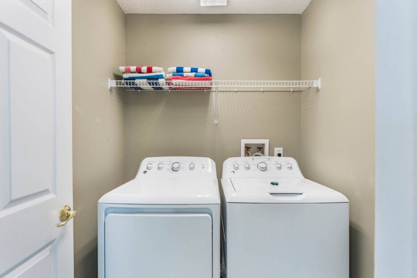 A laundry room with two white front-loading washers and a shelf above holding folded towels.