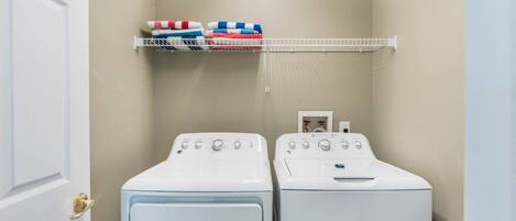 A laundry room with two white front-loading washers and a shelf above holding folded towels.