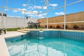 Piscina com borda em azulejos azuis, rodeada por uma cerca branca, e uma mesa com cadeiras do lado de fora.