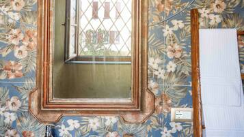 Une salle de bain avec un papier peint à motifs floraux, un miroir encadré en bois, un lavabo blanc et un porte-serviettes.