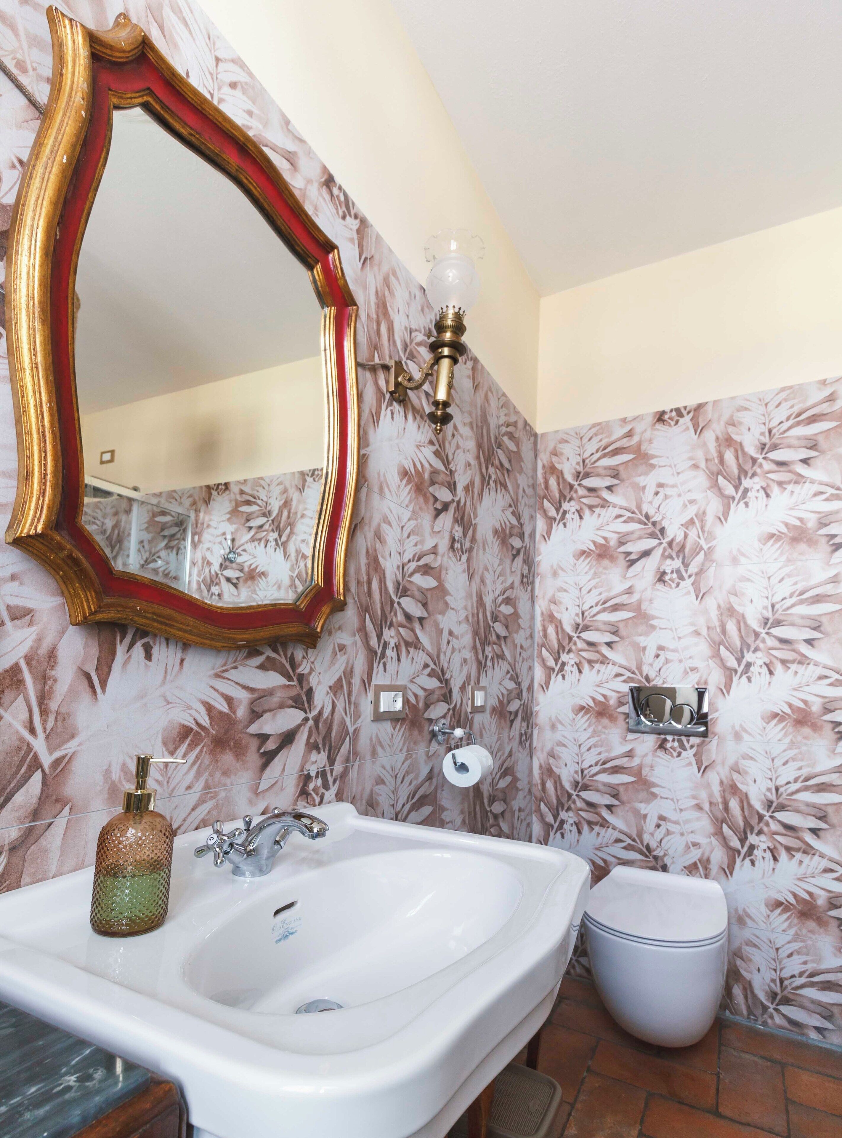 A bathroom with a large mirror, a sink, a toilet, and floral wallpaper.