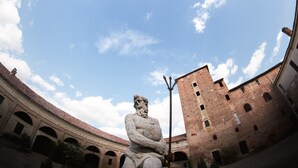 A stone statue in an open courtyard with a clear sky and a brick building in the background. - AGRITURISMO CASTELLO BECCARIA (Pieve del Cairo)