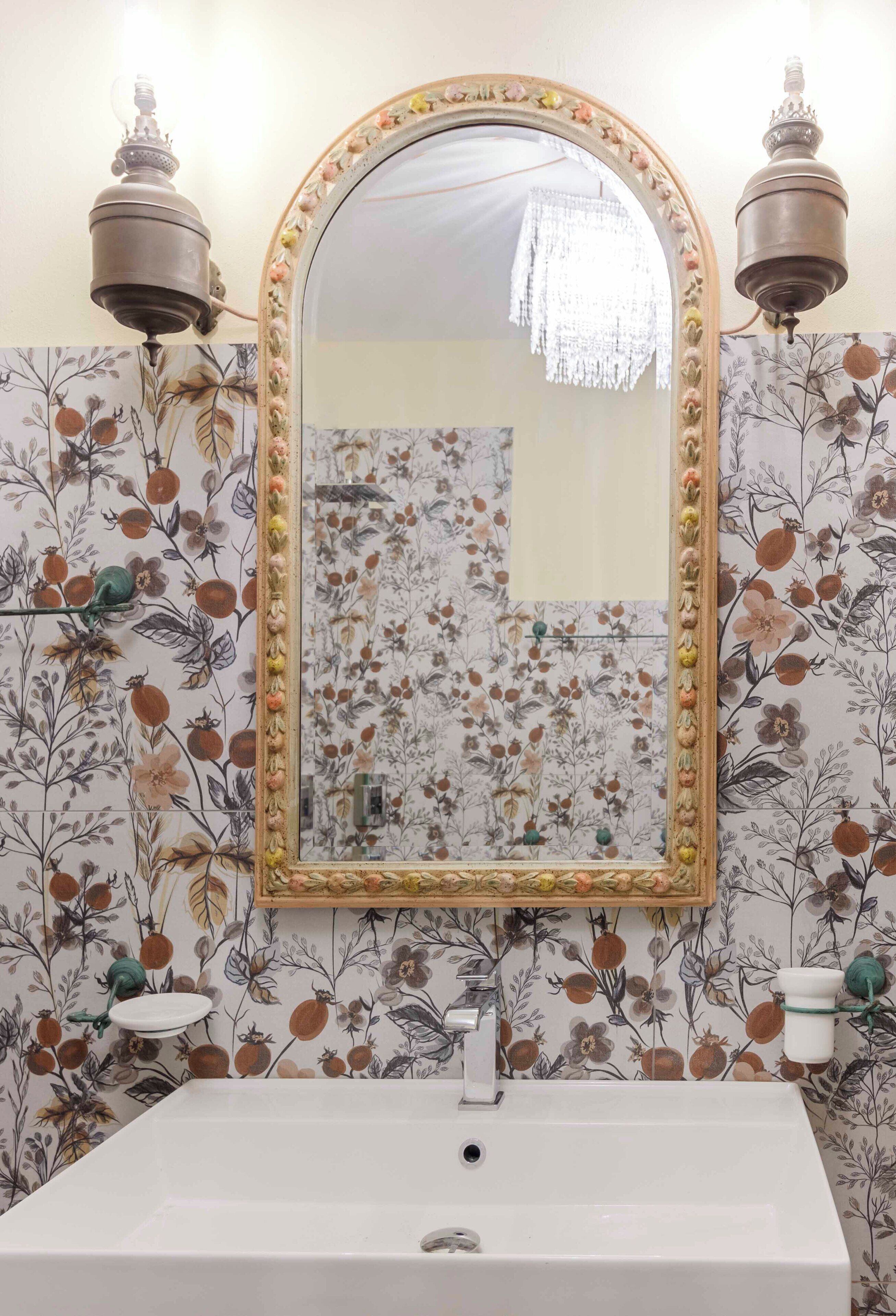 A bathroom with a floral wallpaper, a white sink, and a mirror with a decorative frame.