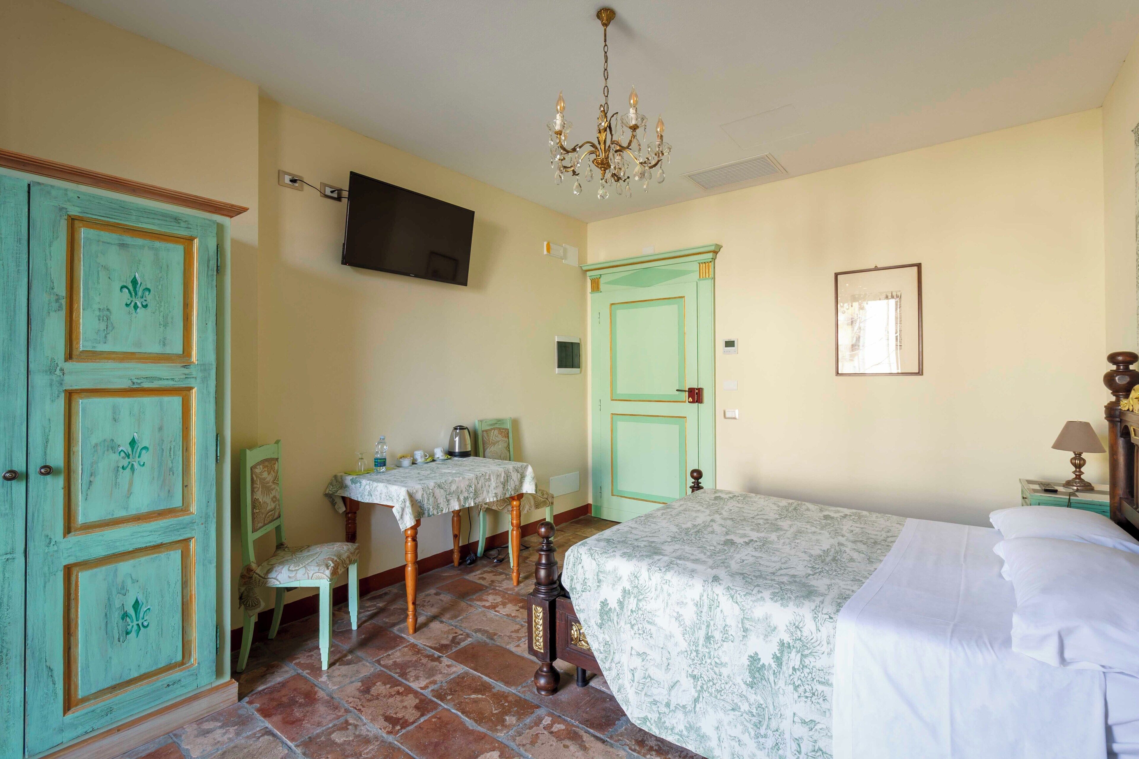 Una stanza con un letto, una scrivania con una sedia, una televisione a parete e un lampadario.