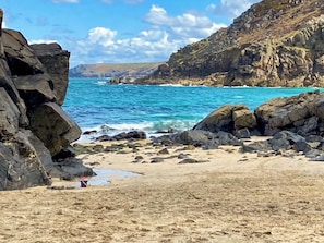 Ein felsiger Strand mit brechenden Wellen, ein klarer Himmel und eine hügelige Landschaft im Hintergrund.