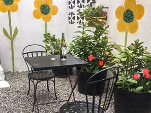 A table with chairs, a bottle, and wine glasses. There are potted plants with red flowers and green foliage. - This cosy cottage is an ideal base for you and your dogs. (St Just)