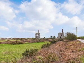 Two stone ruins with chimneys, surrounded by grassy fields and a clear sky. - This cosy cottage is an ideal base for you and your dogs. (St Just)