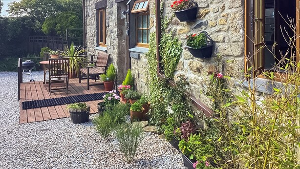 A stone house with a patio, outdoor seating, and potted plants. - This cosy cottage is an ideal base for you and your dogs. (St Just)