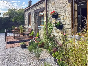 Una casa de piedra con un patio, mobiliario exterior y macetas con plantas.