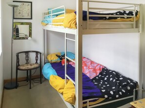 Une chambre avec un lit superposé, une chaise, un tableau encadré et une petite table.