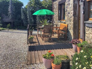 Une terrasse extérieure avec une table et des chaises, un parasol vert et des plantes en pot.