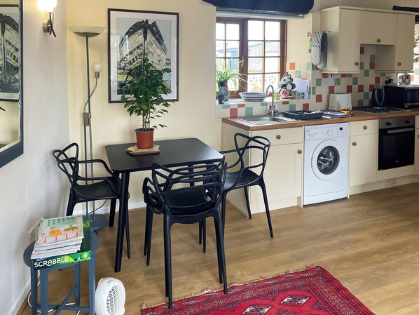 A compact kitchen with a sink, stove, and washing machine, a dining area with chairs and a table, and a potted plant. - This cosy cottage is an ideal base for you and your dogs. (St Just)