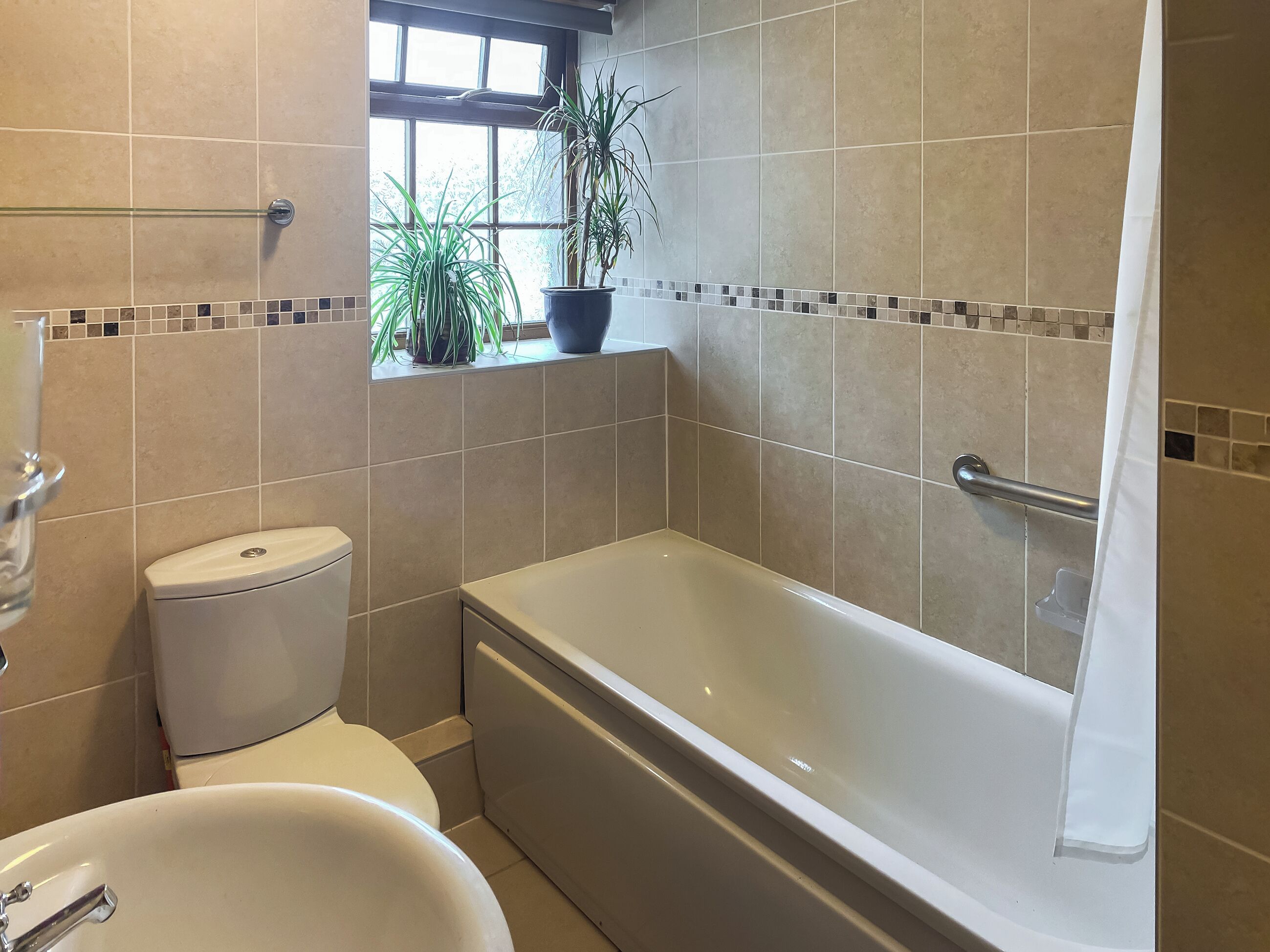 Ein Badezimmer mit Badewanne, Toilette und einem Fenster mit Pflanzen.