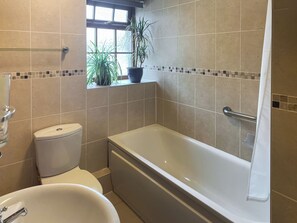 Un baño con bañera, inodoro y ventana con plantas.
