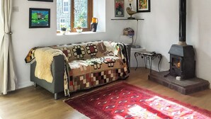A cozy living room with a sofa, a red rug, a fireplace, and various framed artworks on the walls. - This cosy cottage is an ideal base for you and your dogs. (St Just)