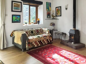A cozy living room with a sofa, a red rug, a fireplace, and various framed artworks on the walls.