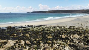 A beach with rocky foreground, sandy shore, and calm sea under a clear sky. - This cosy cottage is an ideal base for you and your dogs. (St Just)