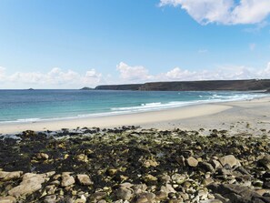 A beach with rocky foreground, sandy shore, and calm sea under a clear sky. - This cosy cottage is an ideal base for you and your dogs. (St Just)