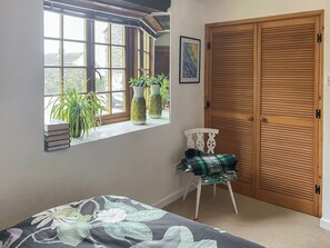 Un dormitorio con ventana, una silla, una cama y una puerta de madera.