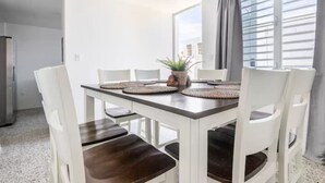 Uma sala de jantar com uma mesa branca, cadeiras marrom-escuro e um vaso com planta.