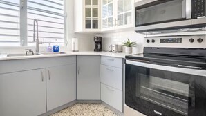 Uma cozinha moderna com armários brancos, micro-ondas, forno, máquina de café e janela com persianas.