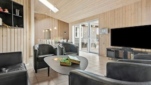 Een moderne woonkamer met houten paneelwanden, een flatscreen televisie, leren banken en een eethoek met stoelen en een tafel.