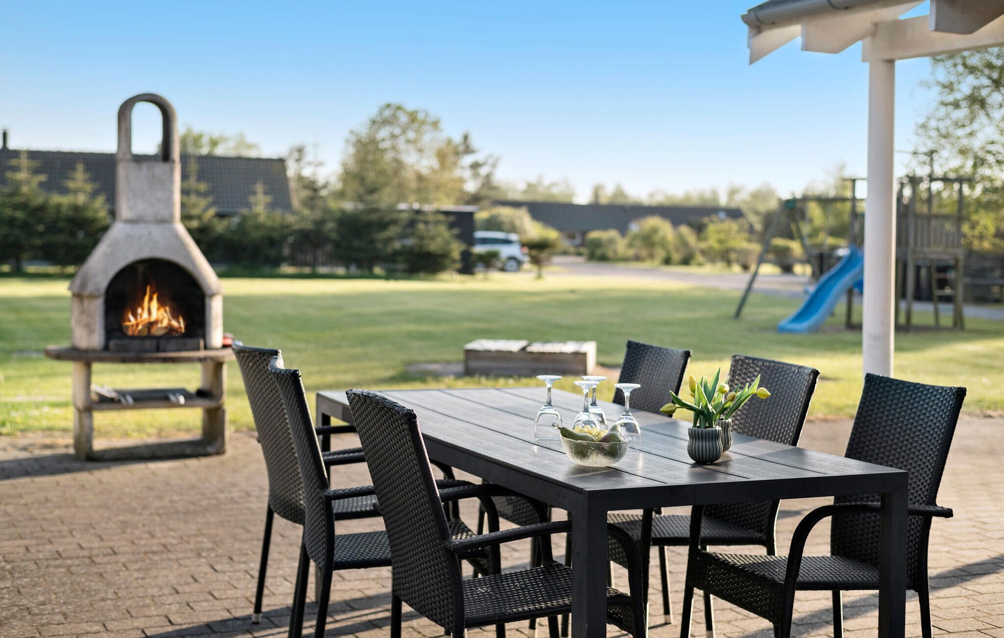 An outdoor patio with a brick table, black wicker chairs, and a stone fire pit.