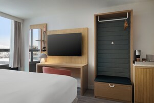 Habitación de hotel con cama, escritorio, televisor, zona de estar y pequeña kitchenette.