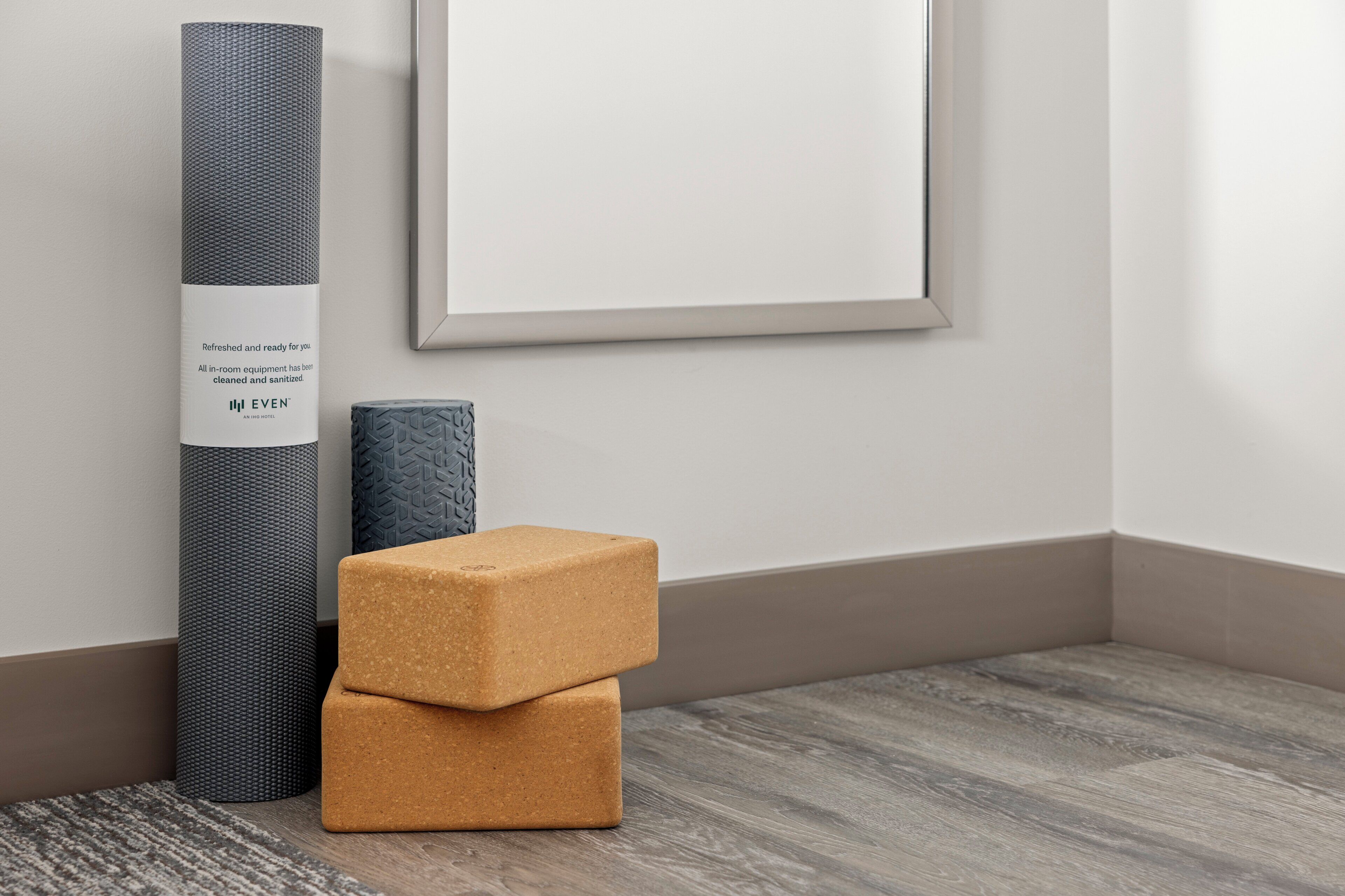 A corner of a room with a grey textured wall, a framed picture, a grey cylindrical object, and two stacked beige cushions.