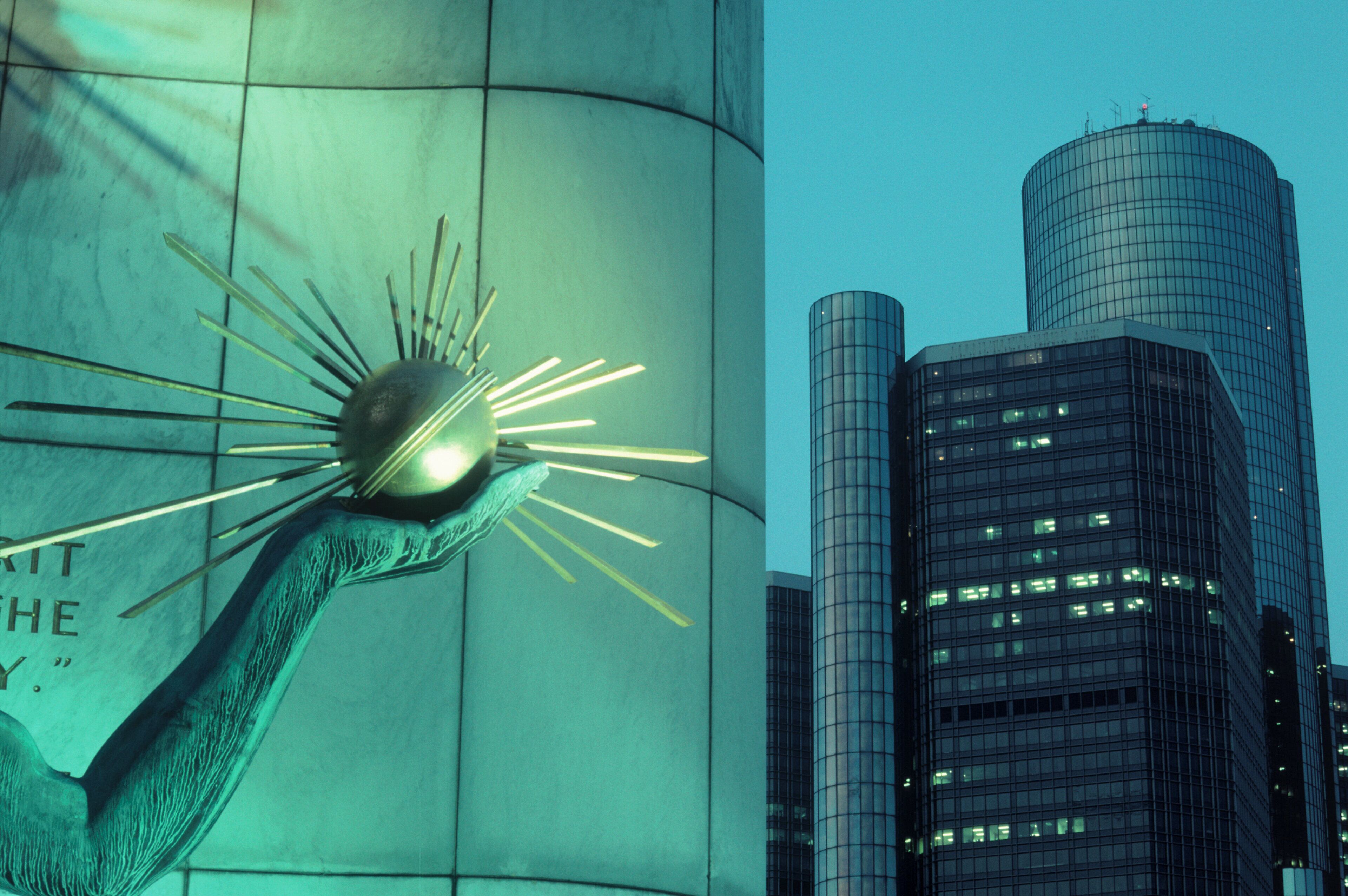 A modern sculpture with a spherical element and radiating lines, set against a backdrop of tall buildings with reflective glass facades.